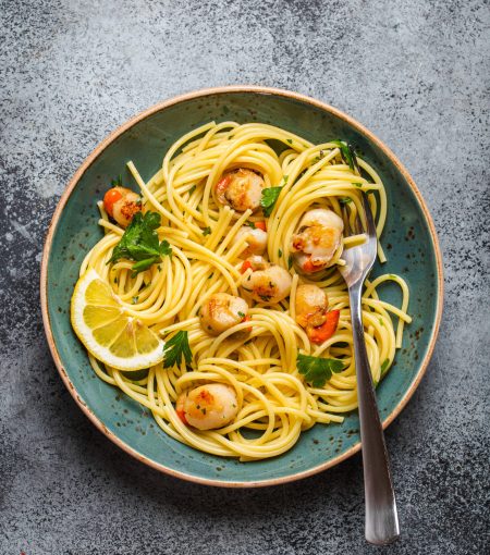 Spaghetti with seafood, delicious fried cooked scallops served on blue plate, grey rustic concrete background, top view, close-up. Seafood pasta concept
